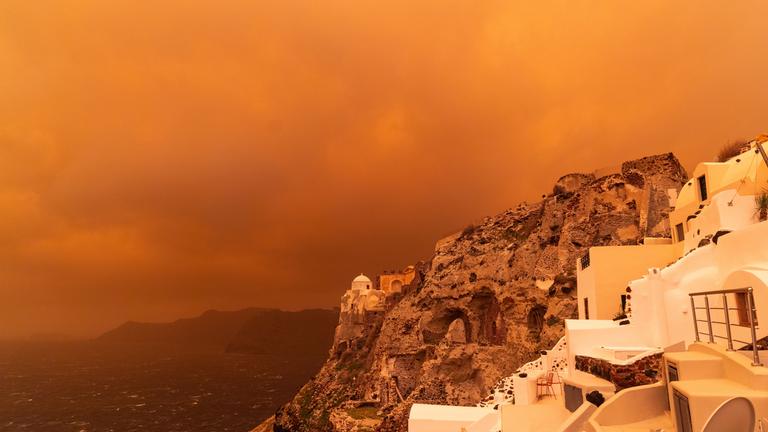 Kräftiger Sturm trägt Sand aus Afrika über die Insel Santorin und färbt den Himmel orangerot ein.
