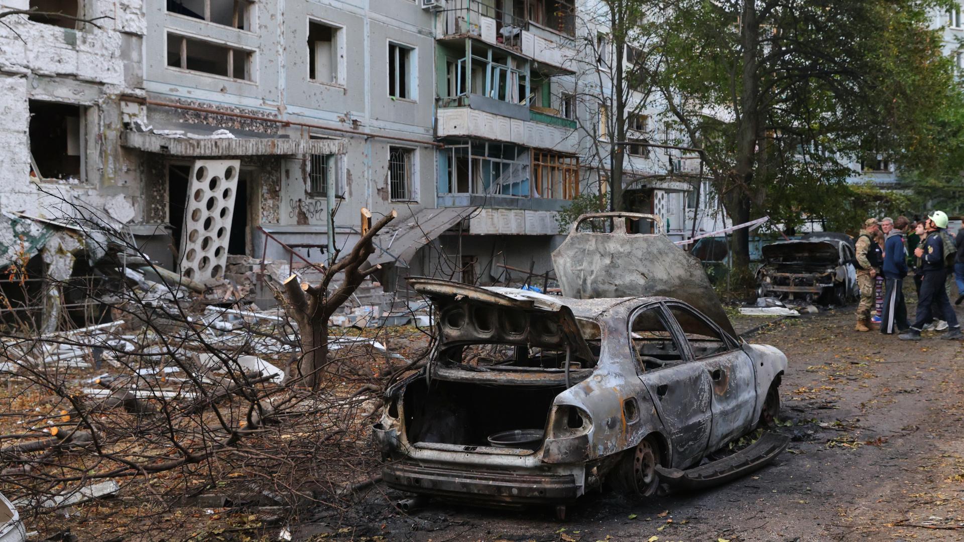 Ein ausgebranntes Auto steht vor einem zerstörten Haus. 