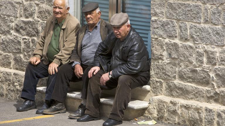 Drei ältere Männer sitzen auf Stufen und beobachten die Straße.