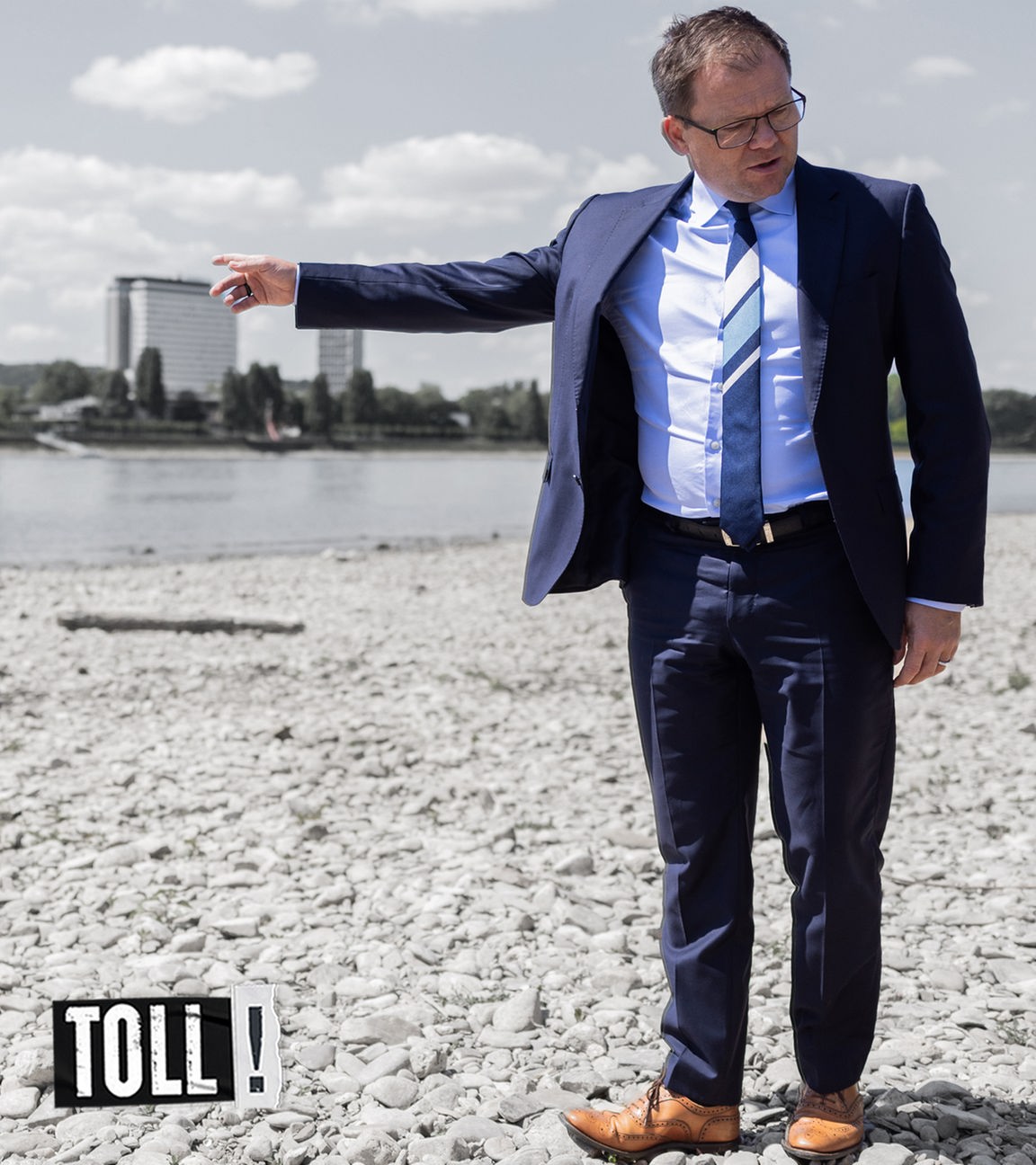 Bundesumweltminister Carsten Schneider zeigt auf einen Fluss mit Niedrigpegelstand