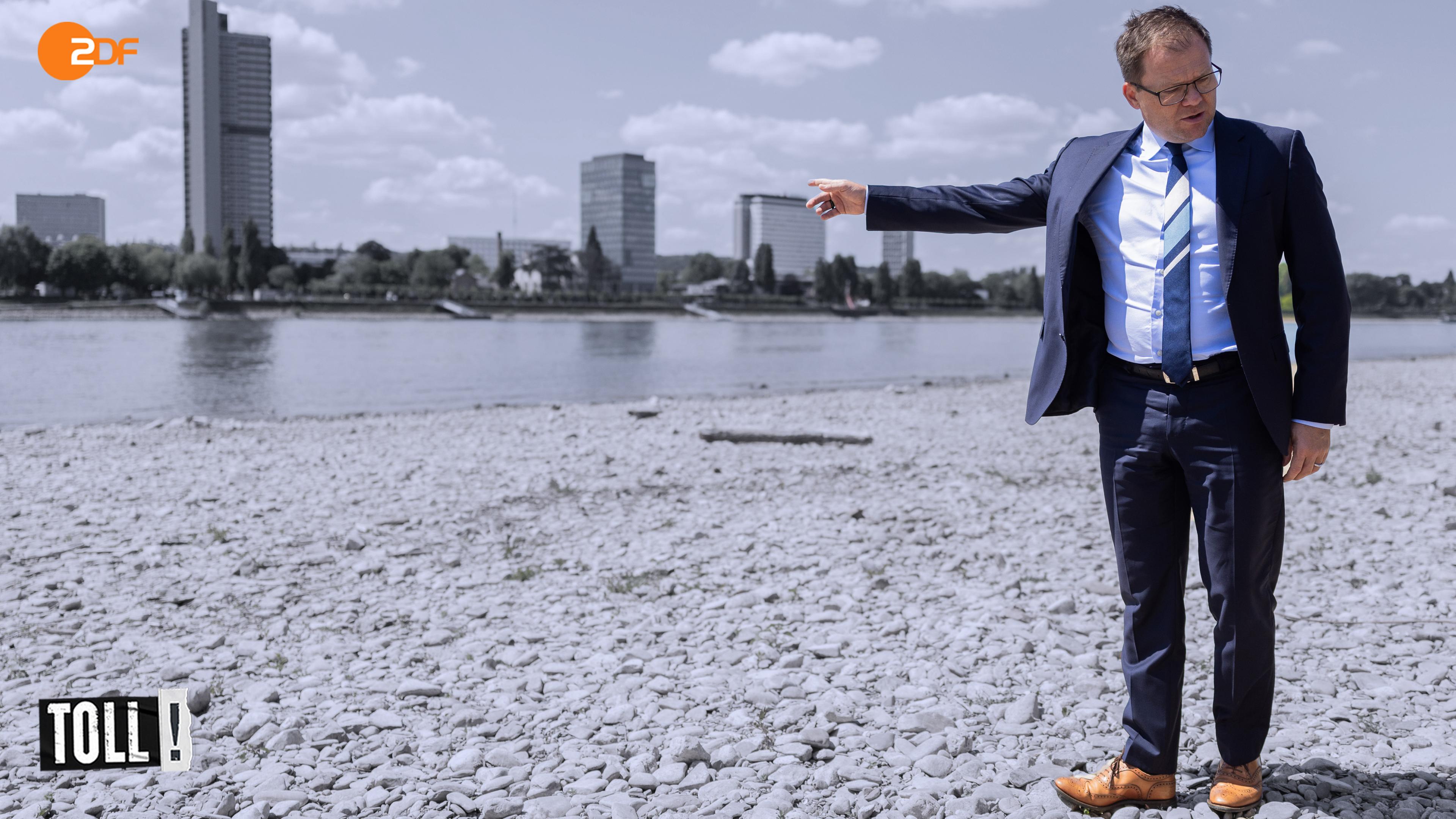 Bundesumweltminister Carsten Schneider zeigt auf einen Fluss mit Niedrigpegelstand