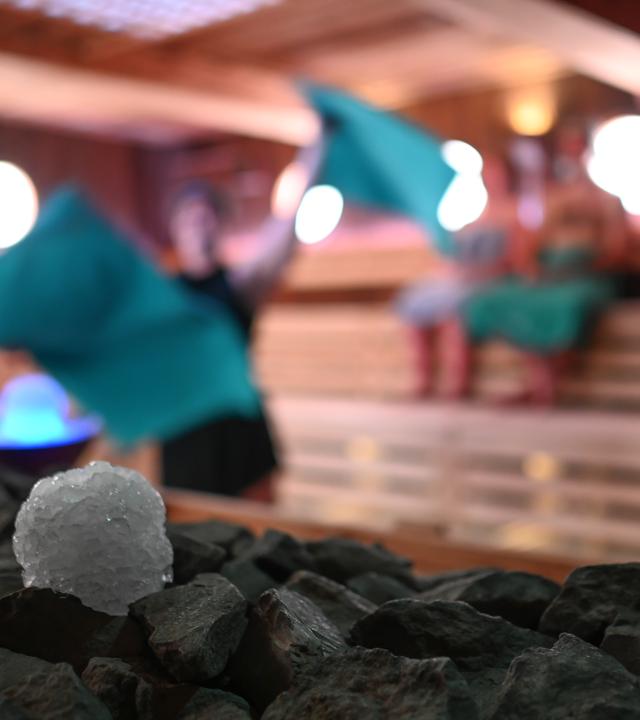 Schneebälle aus Crushed Ice liegen in der Koggen-Sauna in Ostfriesland neben einem Sauna-Ofen für einen Event-Aufguss bereit. Eine Mitarbeitern schwingt das Handtuch für die Luftverteilung in der Sauna.