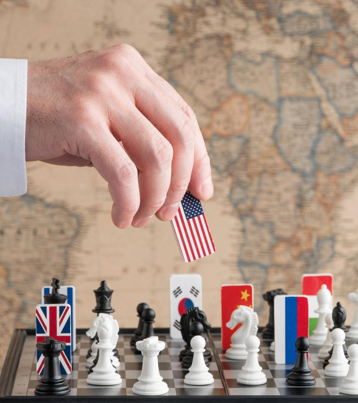 Eine Hand nimmt eine Spielfigur mit US-amerikanischer Flagge von einem Schachspiel, auf dem Länderflaggen verteilt sind.