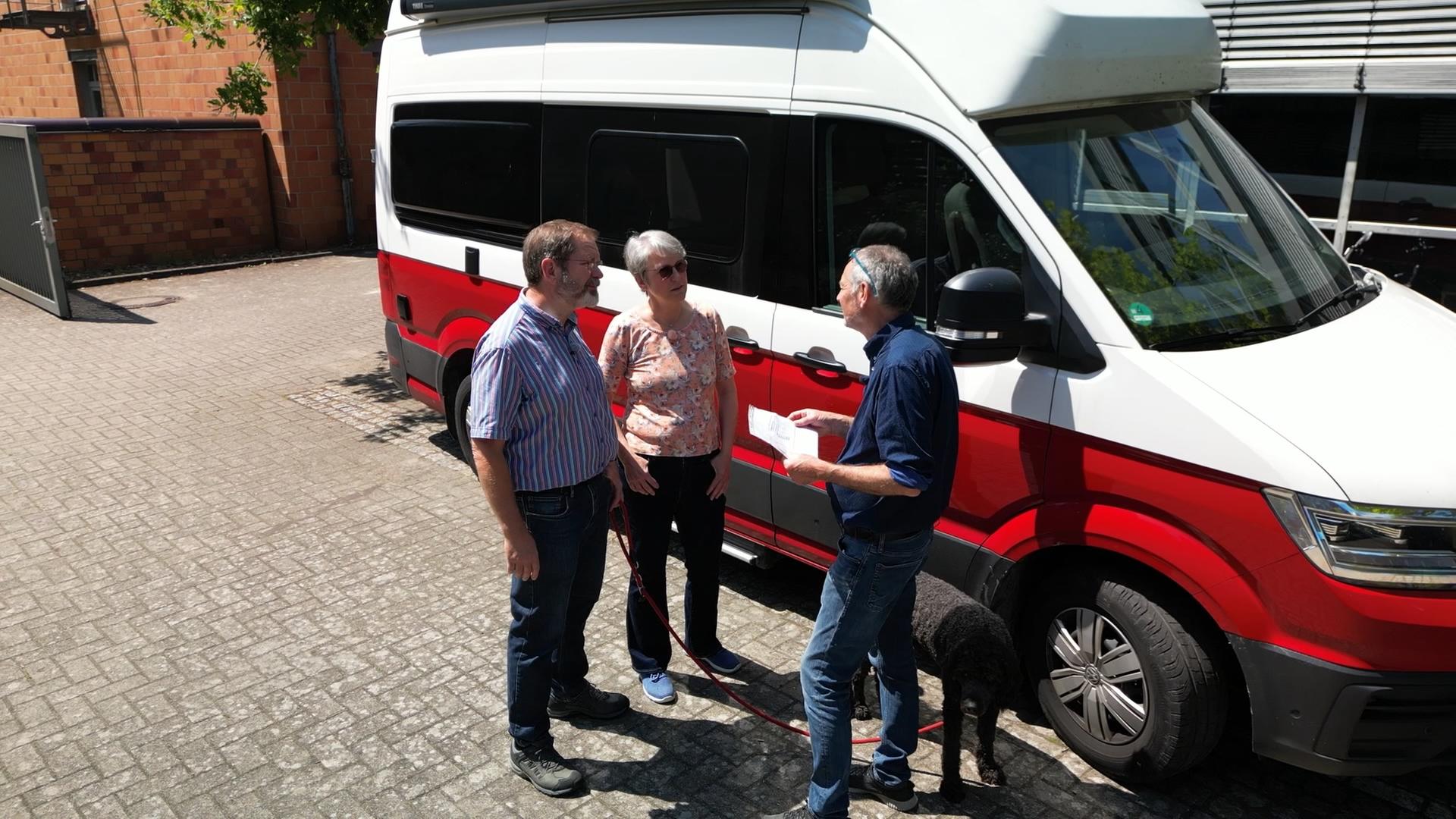 Das Ehepaar Lotter im Gespräch mit einem Experten vor ihrem Campingbus VW Grand California.  