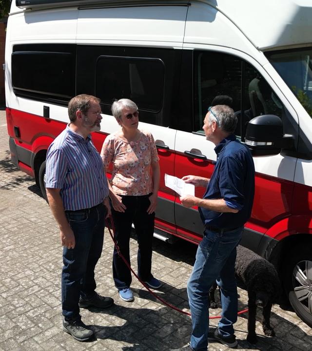 Das Ehepaar Lotter im Gespräch mit einem Experten vor ihrem Campingbus VW Grand California.  