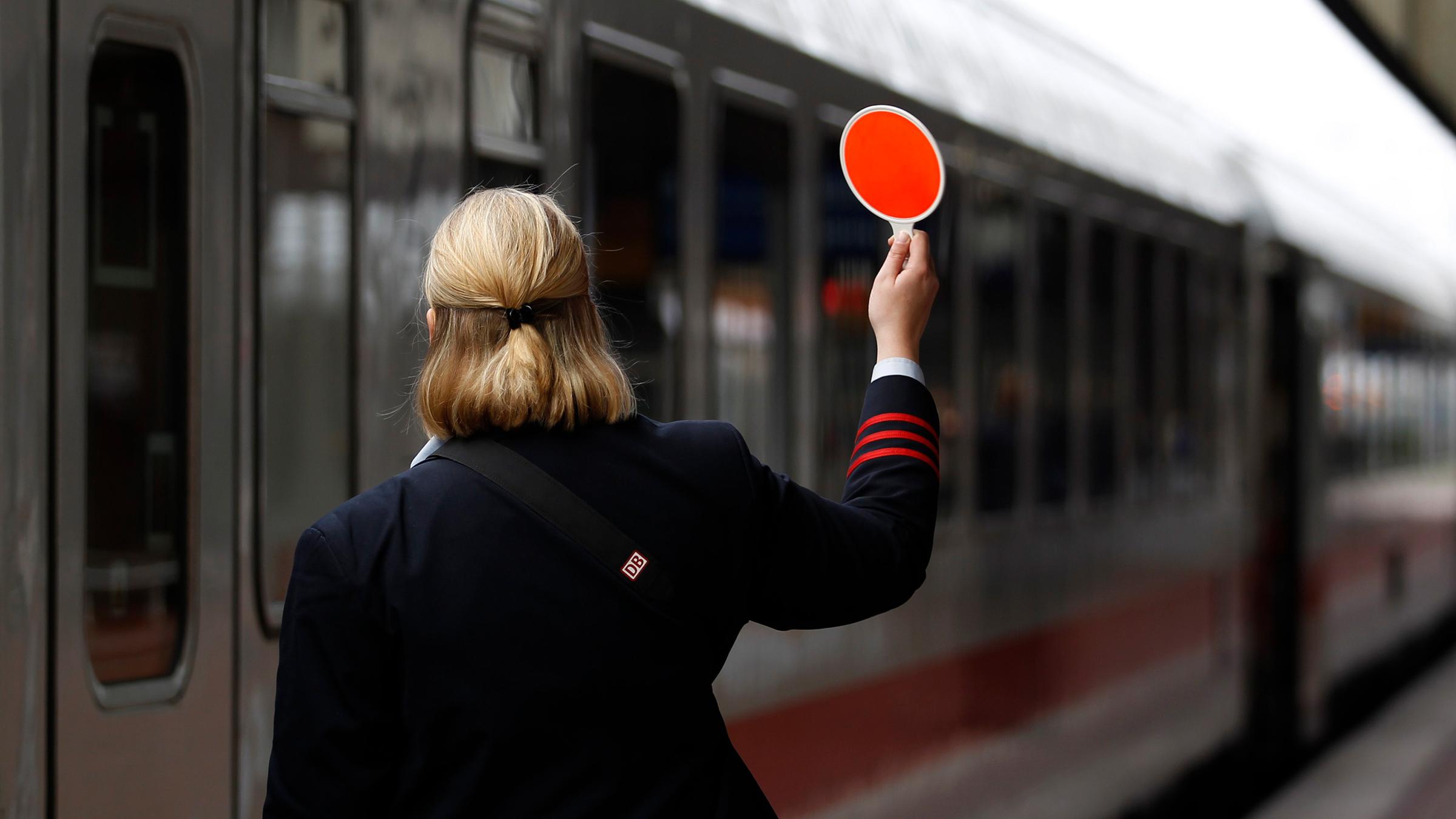 Schaffnerin hält rote Kelle am Bahnsteig hoch