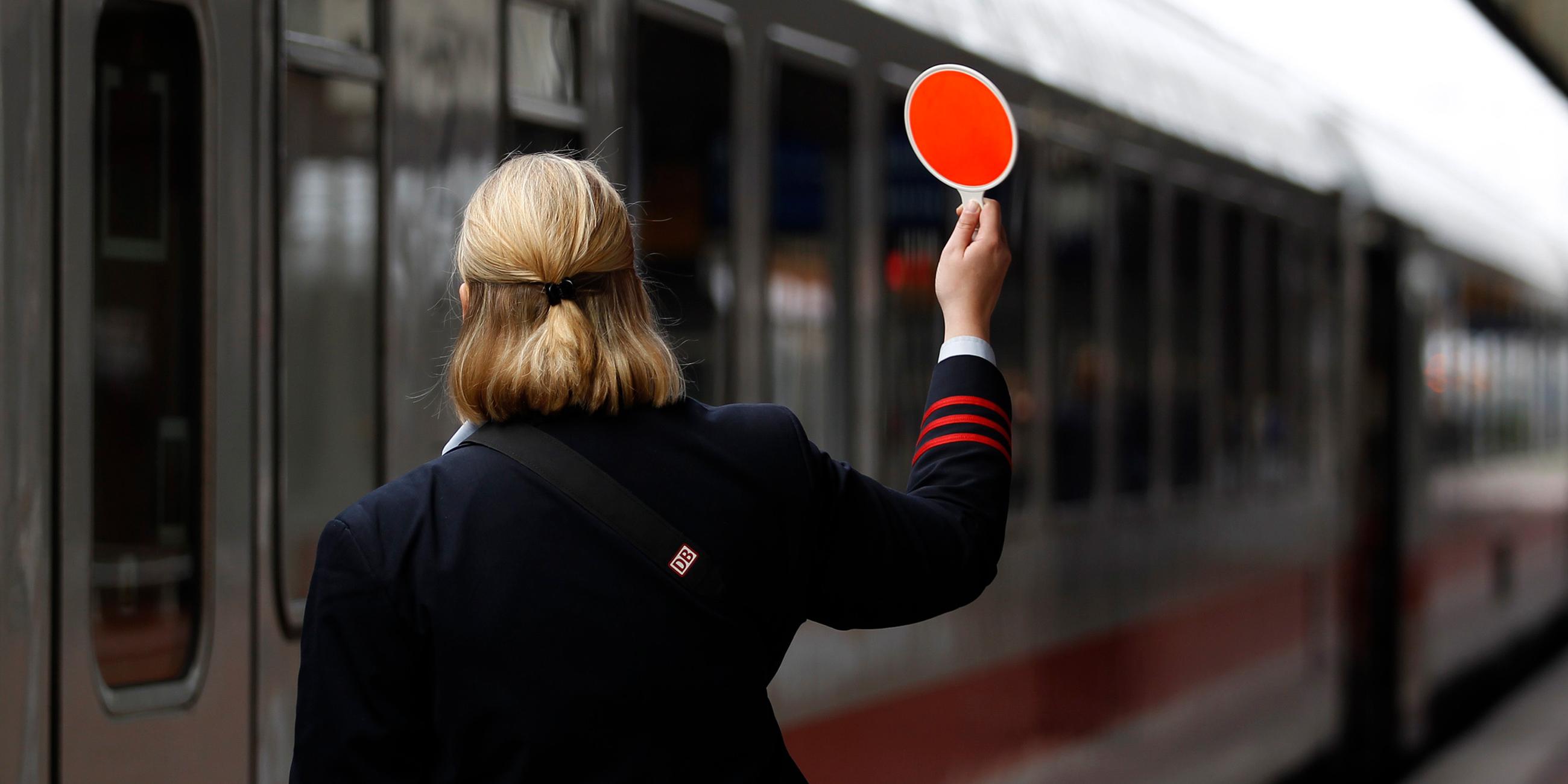 Schaffnerin hält rote Kelle am Bahnsteig hoch