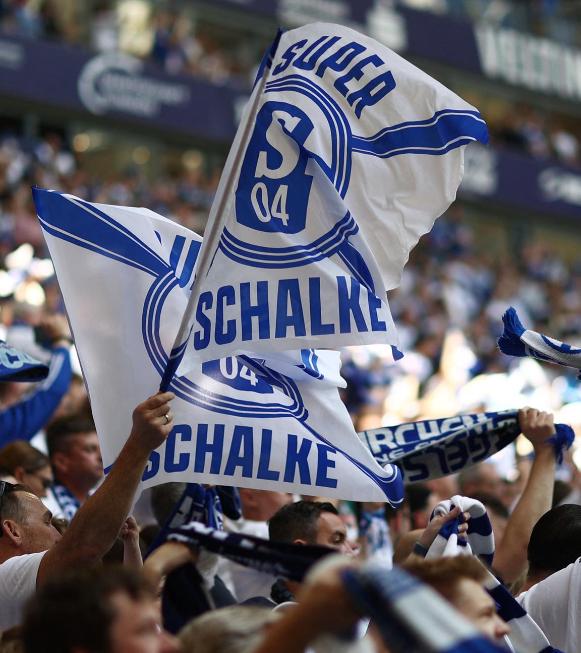 In einem Stadion steht eine Menschenmenge und hält blau-weiße Schalke Fahnen und Schals.