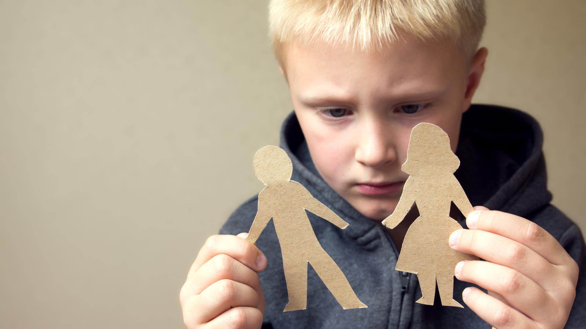 Ein Junge hält zwei Papierfiguren in den Händen, die einen Mann und eine Frau darstellen.