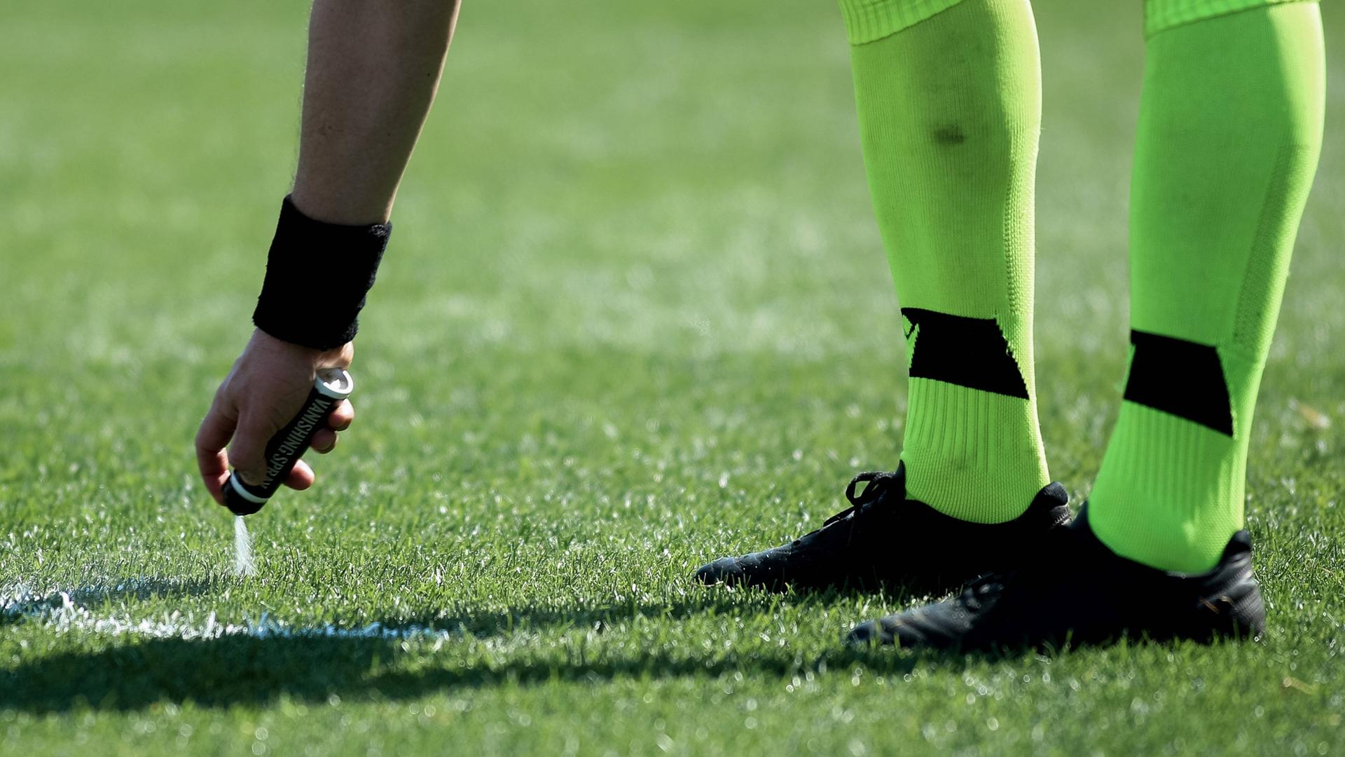 Ein Schiedsrichter sprüht die Freistoßlinie mit Sprühschaum auf den Rasen