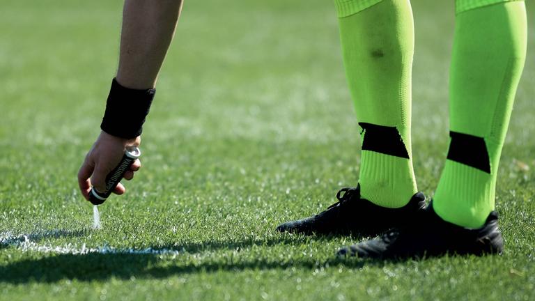 Ein Schiedsrichter sprüht die Freistoßlinie mit Sprühschaum auf den Rasen