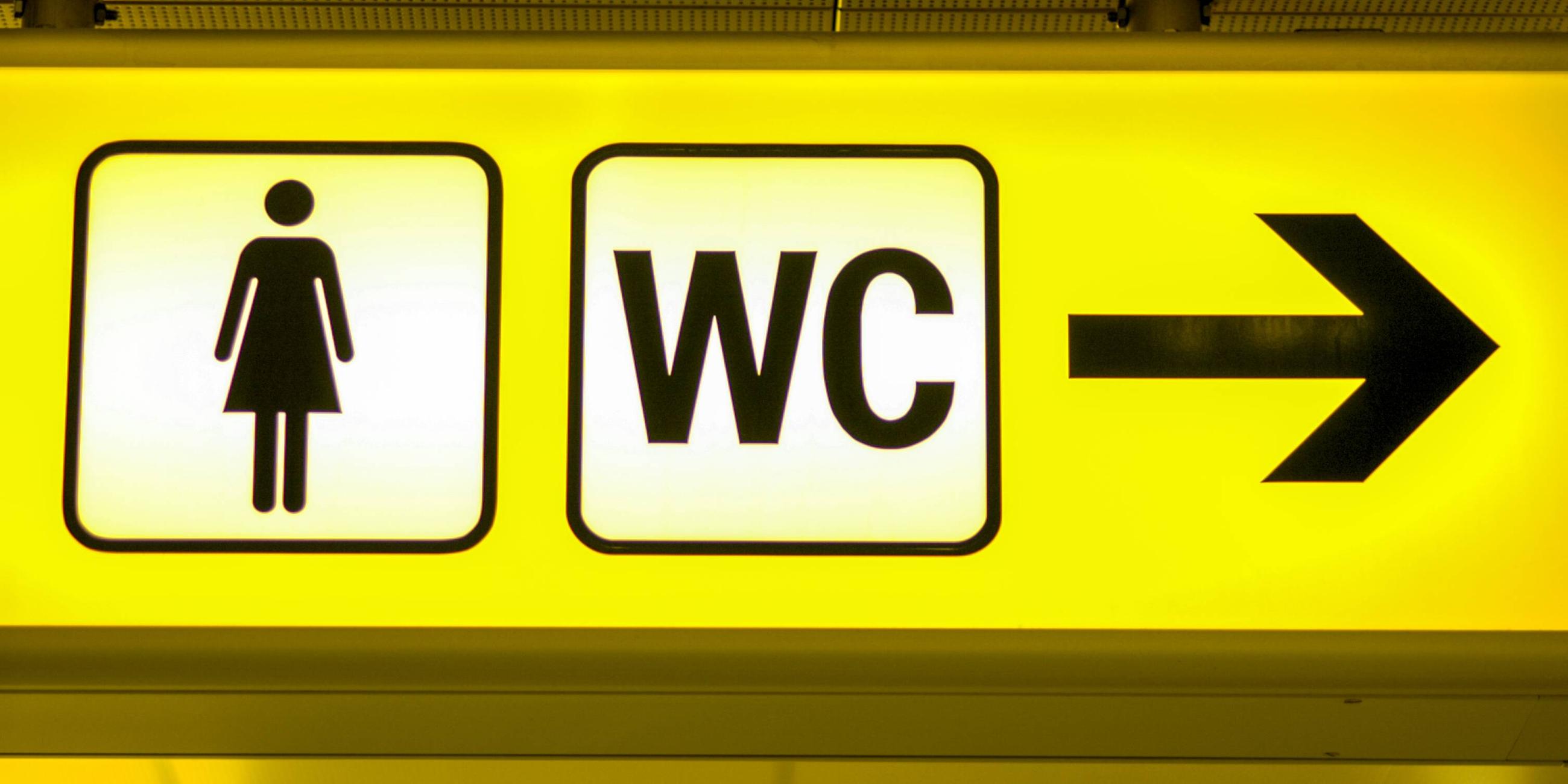 Großaufnahme eines gelben Hinweis-Schildes WC mit Pfeil in Richtung der Damentoilette.
