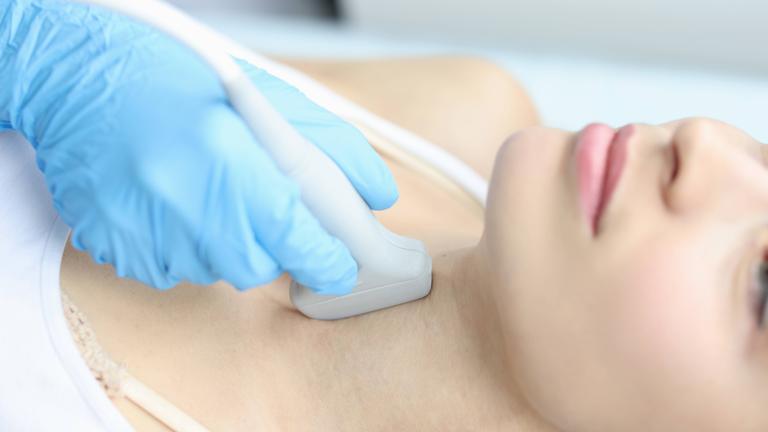 Die Schilddrüse einer Frau wird mit einem Ultraschallkopf untersucht.