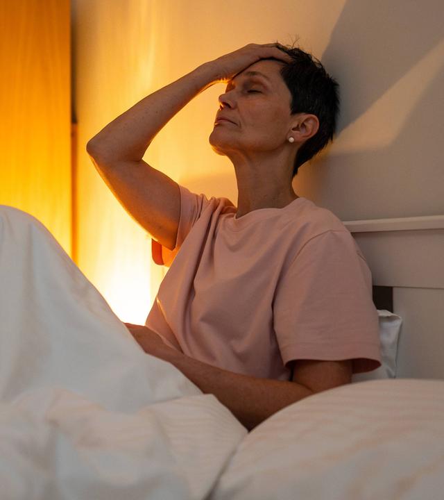 Eine erschöpfte, nachdenkliche ältere Frau mit Schlafstörungen sitzt mit müdem Gesichtsausdruck im Bett.