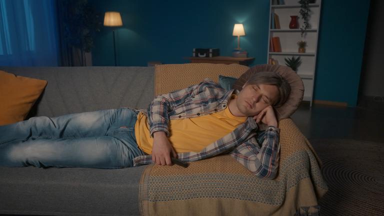 Ein Mann schläft vor dem Fernseher auf einem Sofa.