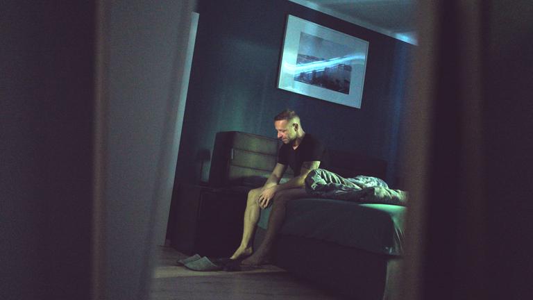 Der 36-jährige Waldemar sitzt auf der Bettkante im dunklen Schlafzimmer und schaut nach unten.