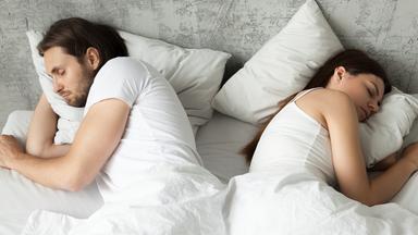 Es sind eine Frau und ein Mann zu sehen, wie sie im Bett liegen und schlafen.