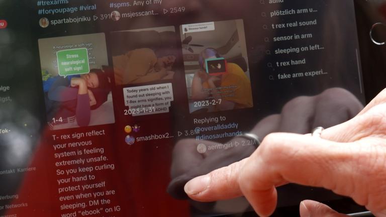 Ein Finger scrollt über einen Bildschirm mit TikTok Videos zu T-Rex-Armen als ungesunde Schlafposition.