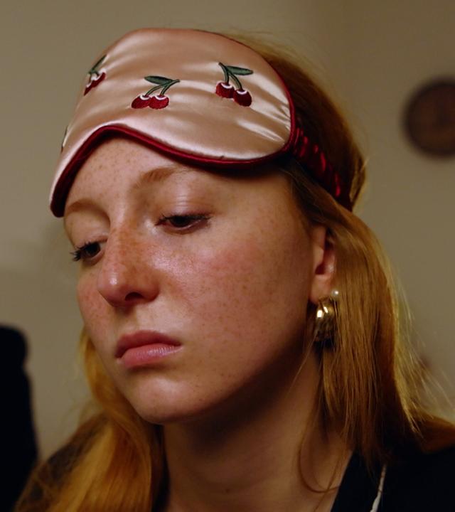 Ein Mädchen hat eine Schlaf-Augenmaske auf der Stirn und schaut betrübt.