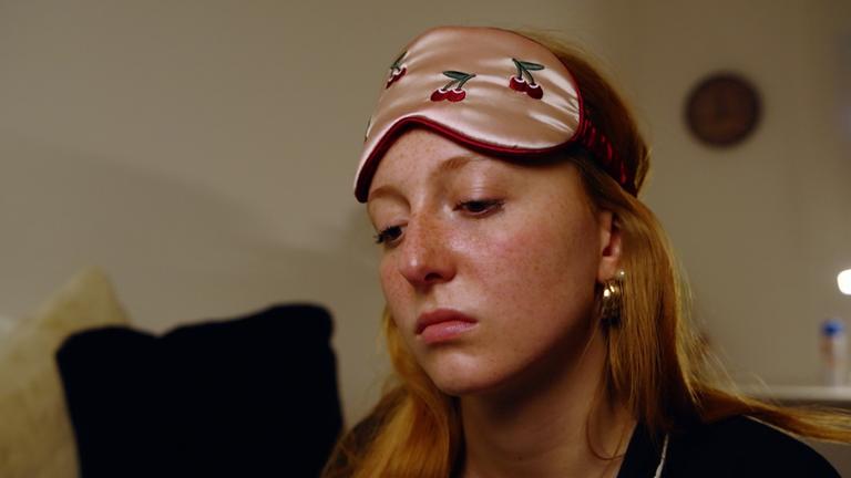 Ein Mädchen hat eine Schlaf-Augenmaske auf der Stirn und schaut betrübt.