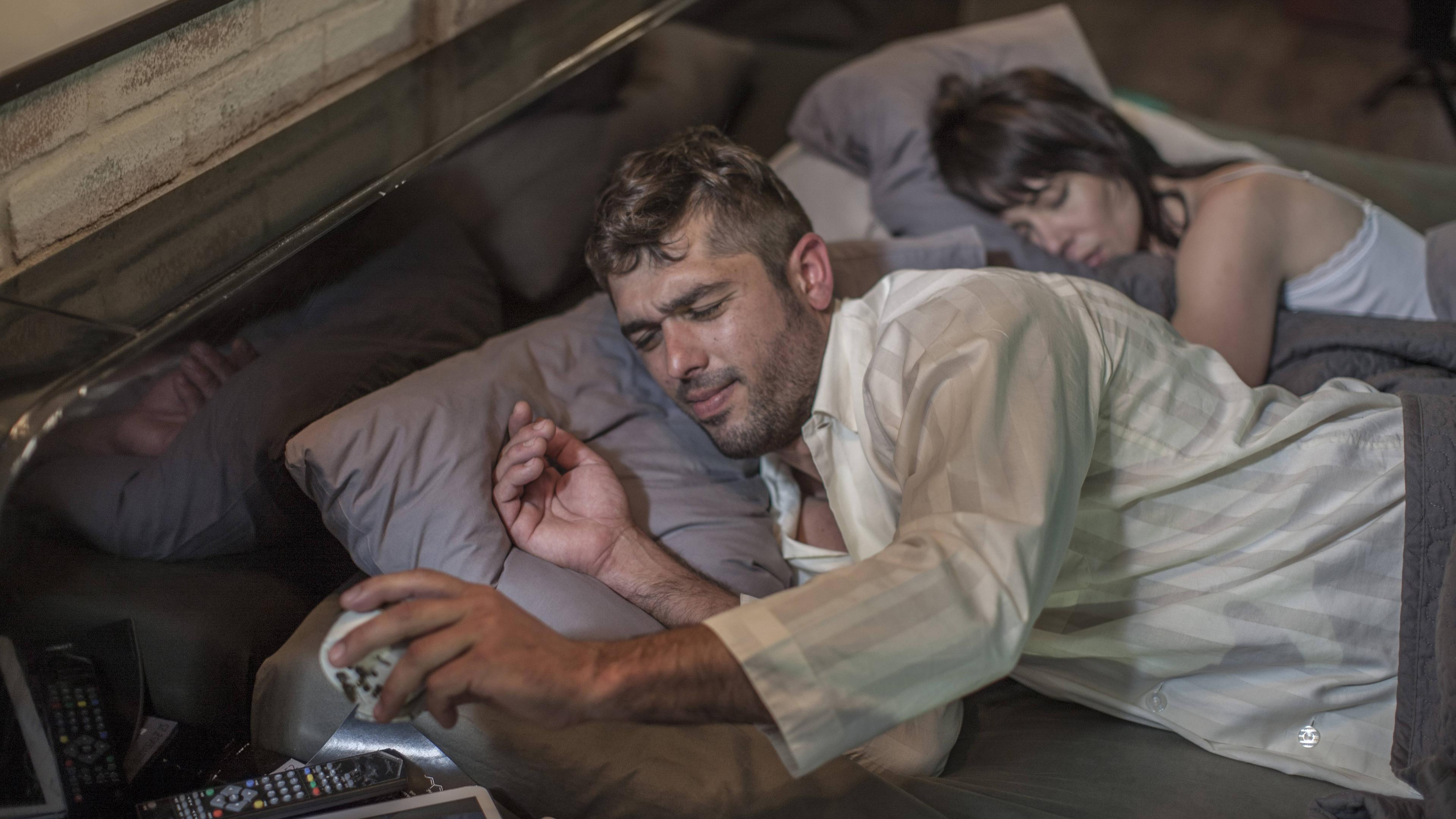 Mann liegt wach im Bett und schaut auf den Wecker, während seine Frau neben ihm schläft.