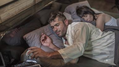 Mann liegt wach im Bett und schaut auf den Wecker, während seine Frau neben ihm schläft.