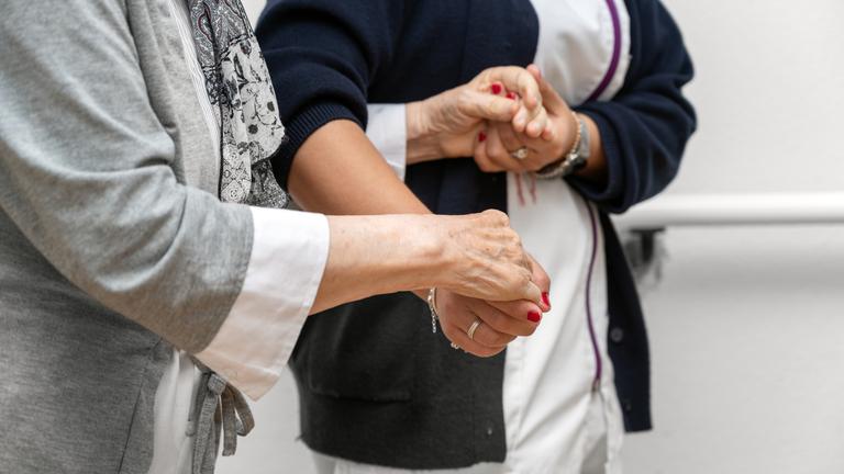 Eine Pflegerin hält eine Patientin unterstützend an den Händen.