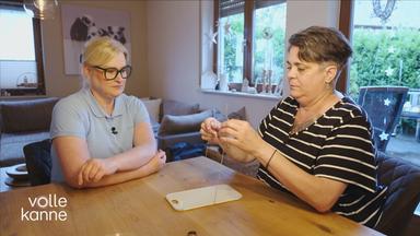 Schlaganfall-Lotse sitzt am Tisch mit Schlaganfall-Patientin und zeigt ihr, wie man eine Schleife bindet.