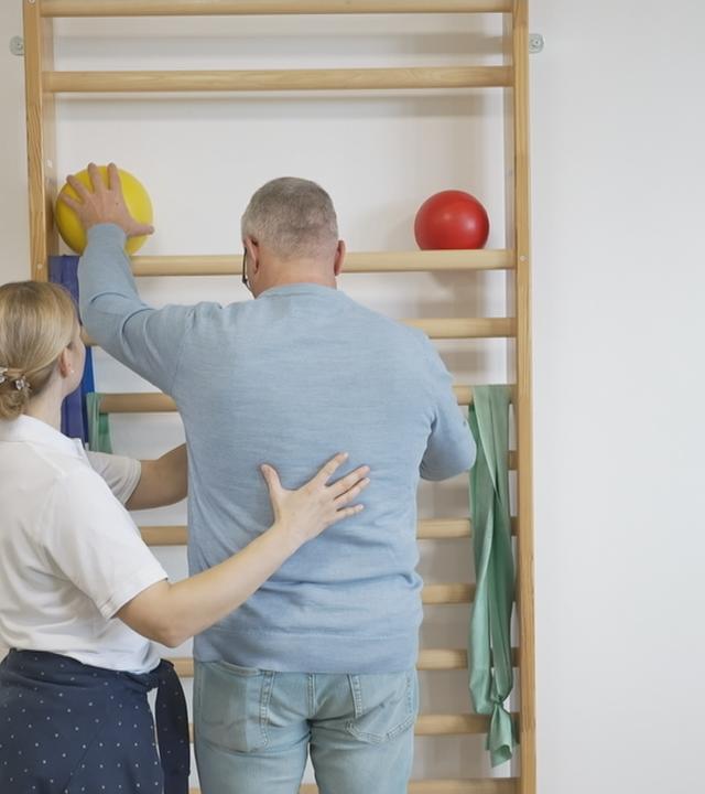 Eine Frau hilft einem Mann bei Krankengymnastik-Übungen.