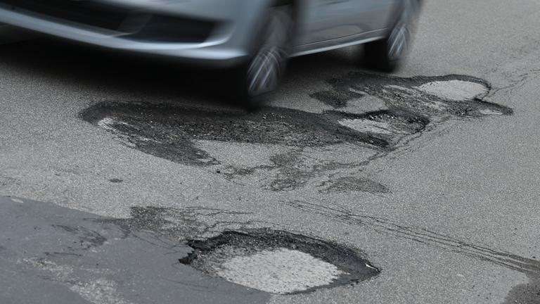 Ein Auto fährt auf einer Straße mit Schlaglöchern.