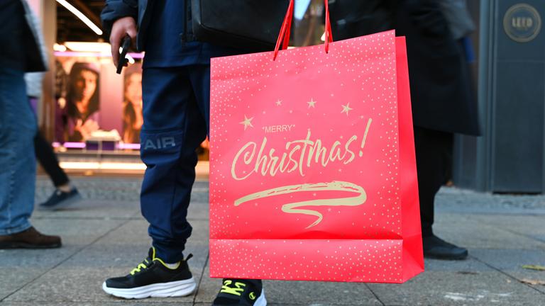 Ein Mann steht mit einer weihnachtlichen Verkaufstüte mit dem Spruch «Merry Christmas» auf einer Einkaufsstraße