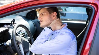 Ein Autofahrer greift sich mit schmerzverzerrtem Gesicht in den Nacken.