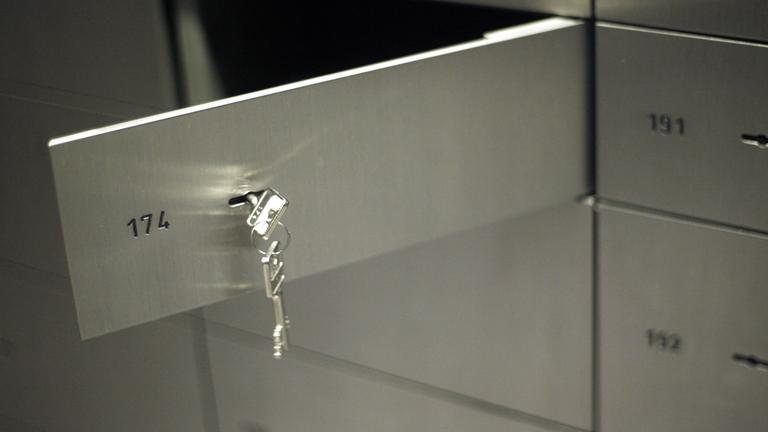 Ein Schließfach in einer Bank steht offen. An dem Fach hängt ein Schlüssel.