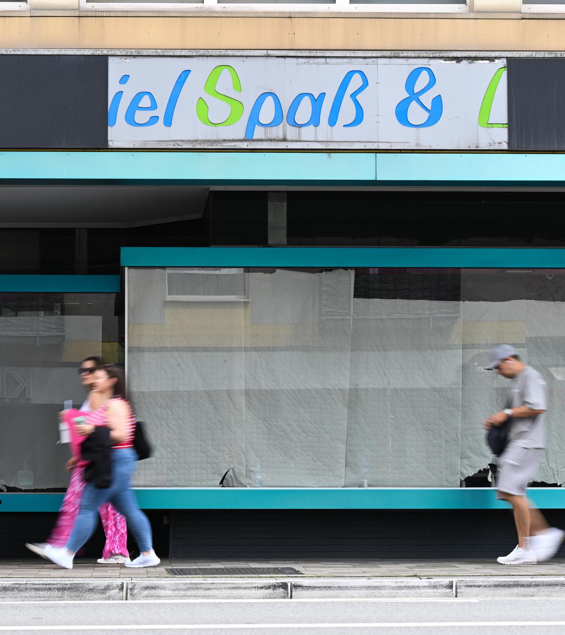 Menschen gehen in Mainz an einem leerstehenden Ladengeschäft vorbei, dessen Schaufenster mit Papierbahnen zugehängt sind 