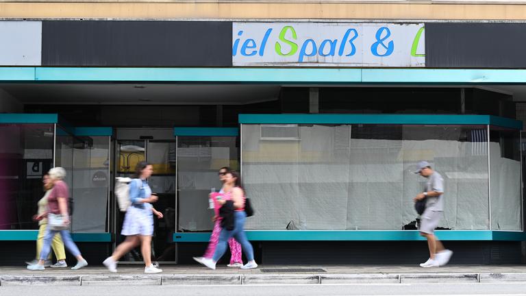 Menschen gehen in Mainz an einem leerstehenden Ladengeschäft vorbei, dessen Schaufenster mit Papierbahnen zugehängt sind 