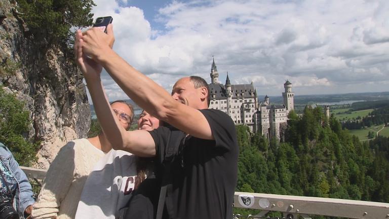 Touristen machen Selfie auf Brücke mit Schloss Neuschwanstein im Hintergrund