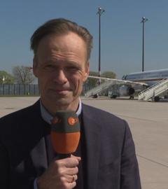 Wulf Schmiese ist mit einem Mikrofon zu sehen, im Hintergrund ist eine Fluglandebahn mit Flugzeug zu sehen.