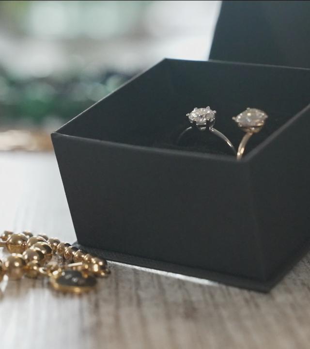 Zwei Silberringe und eine goldene Perlenkette liegen auf einem Tisch.