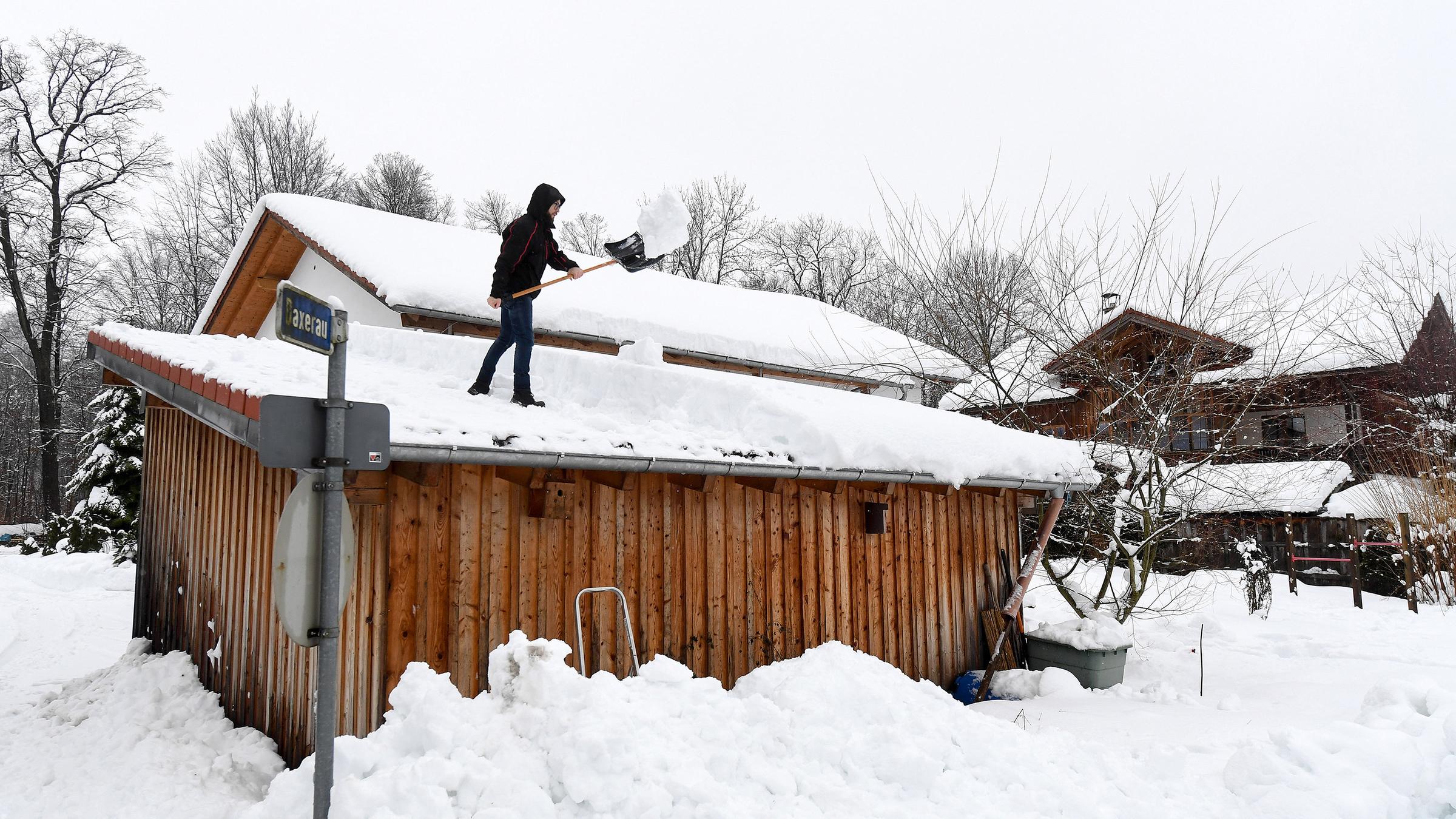 Ein Mann befreit ein Dach vom Schnee.