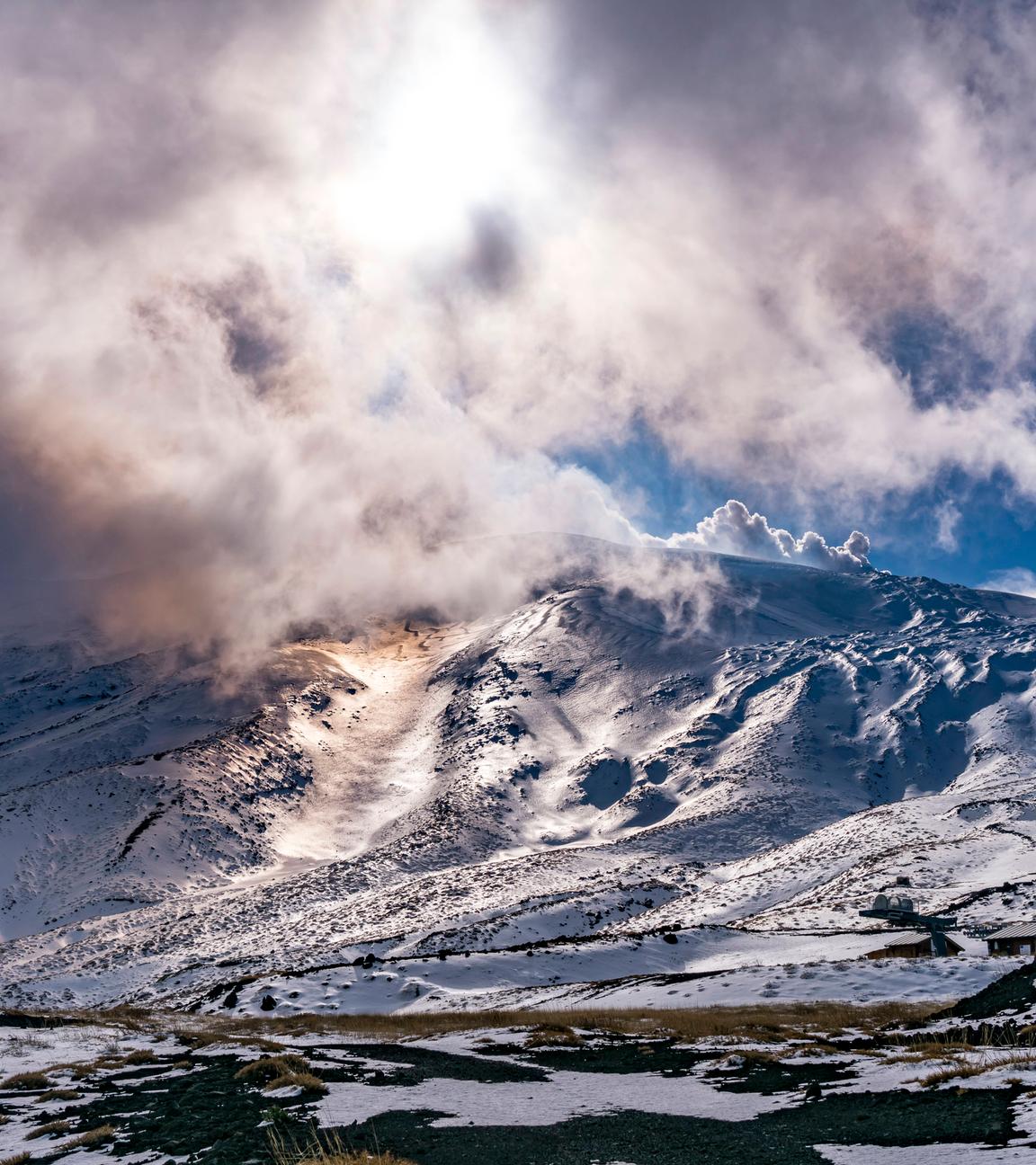 Sonne scheint durch die Wolken über dem schneebedeckten Ätna