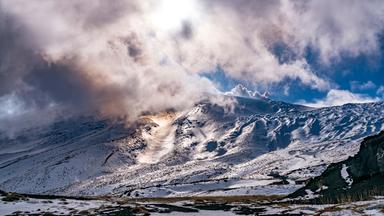 Sonne scheint durch die Wolken über dem schneebedeckten Ätna