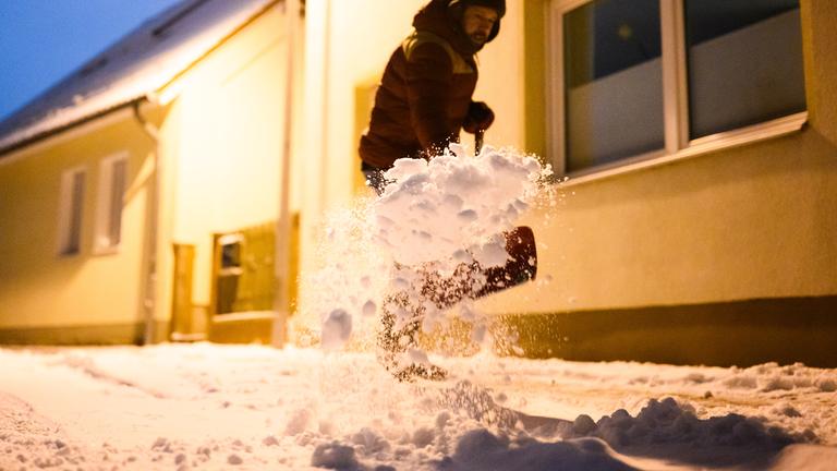 Ein Mann befreit den Gehweg vor seinem Haus von Schnee.