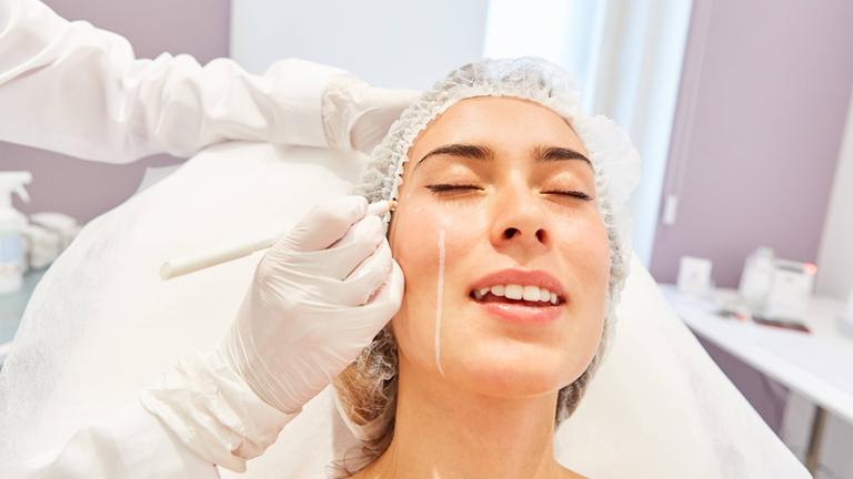 Symbolbild: Arzt markiert Gesichtshaut einer Patientin