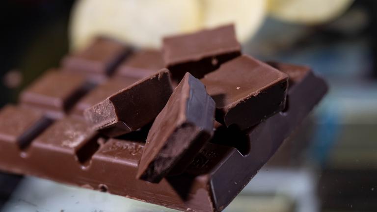 Eine Tafel Schokolade mit vier Reihen liegt auf einem Glastisch. Auf der Tafel liegen vier einzelne Stücke der Schokolade.