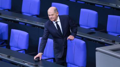 Bundeskanzler Olaf Scholz (SPD) hält sich an einem Stuhl auf der Regierungsbank fest.