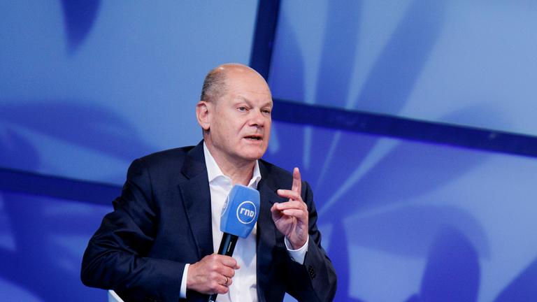 Bundeskanzler Scholz mit Mikrofon und gehobenem Zeigefinger.