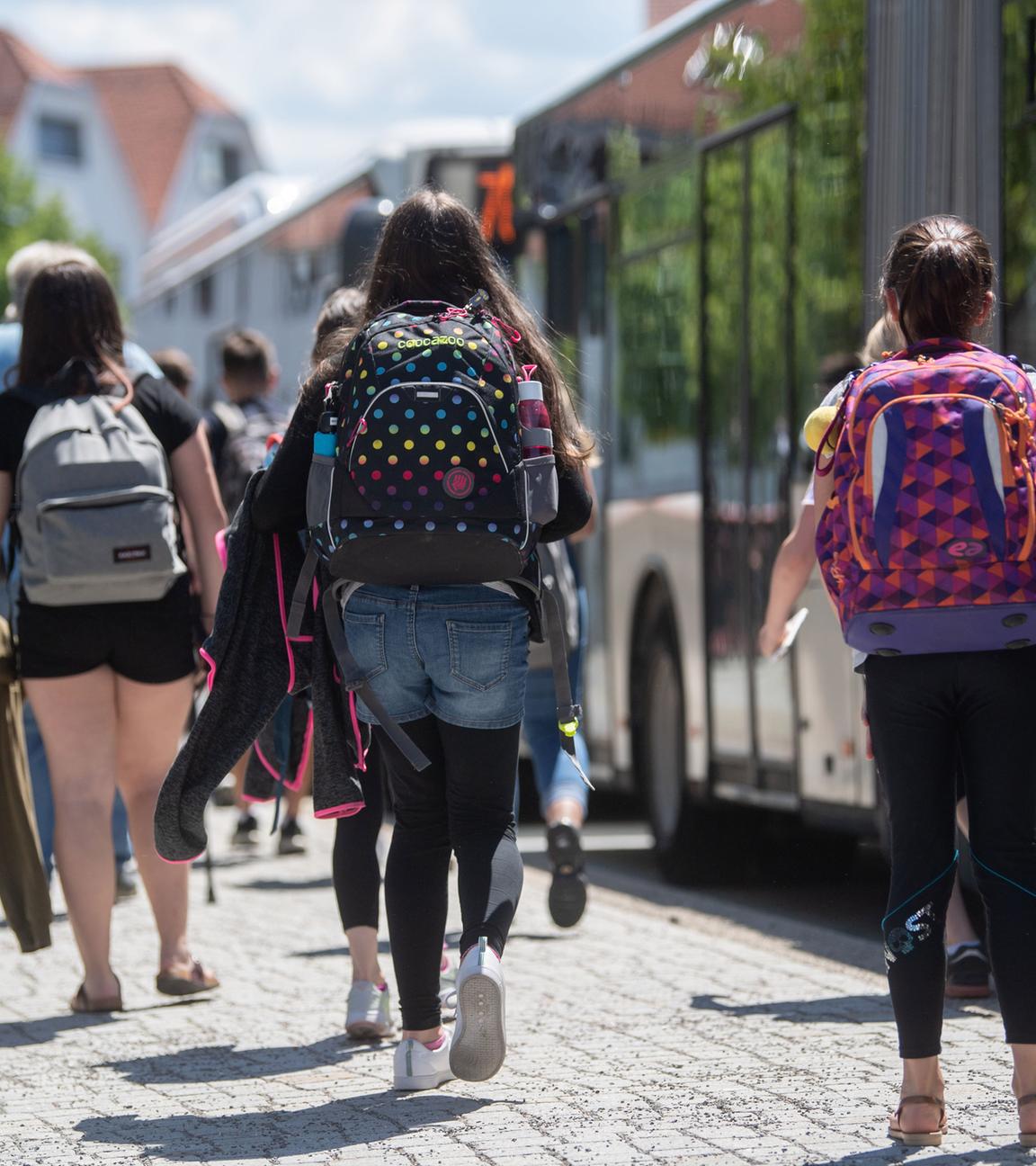 Baden-Württemberg, Rottenburg am Neckar: Schülerinnen gehen an einer Bushaltestelle in der Innenstadt zu stehenden Bussen.