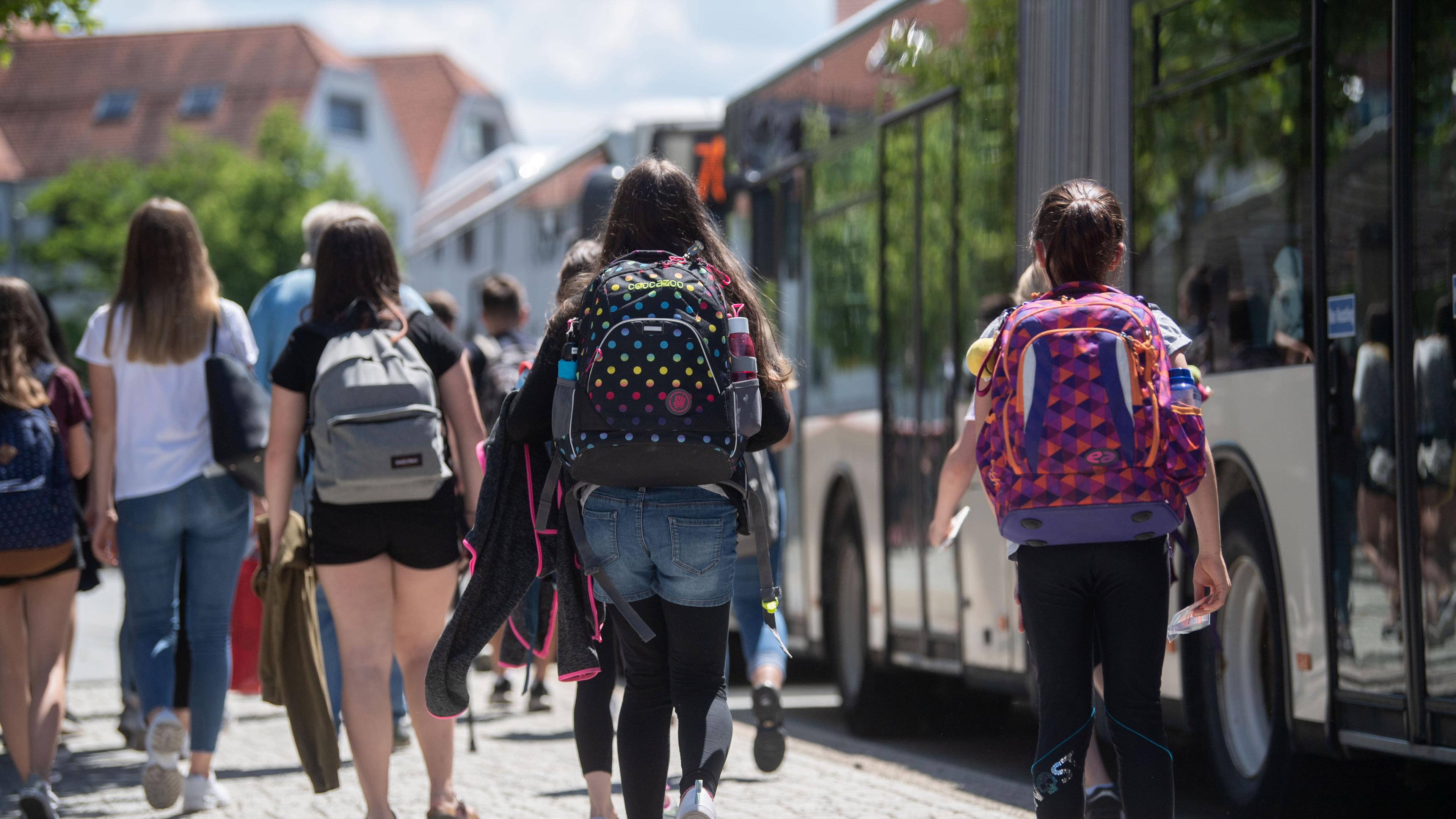 Baden-Württemberg, Rottenburg am Neckar: Schülerinnen gehen an einer Bushaltestelle in der Innenstadt zu stehenden Bussen.