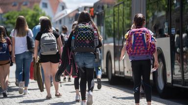 Baden-Württemberg, Rottenburg am Neckar: Schülerinnen gehen an einer Bushaltestelle in der Innenstadt zu stehenden Bussen.