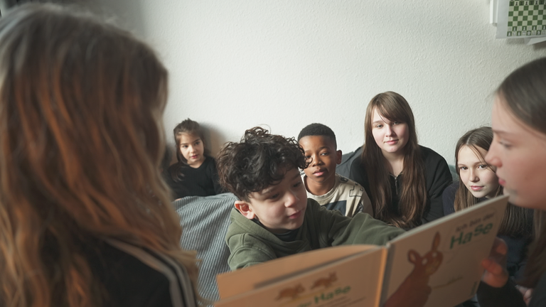 Schüler und Schülerinnen einer Bremer Gesamtschule sitzen zusammen und lesen gemeinsam ein Buch.